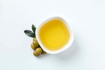 Bowl of fresh olive oil and olives with leaves on white background