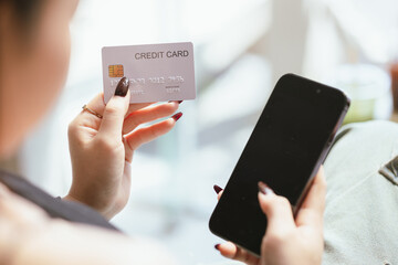 Close-up of young Asian woman using smartphone and credit card for mobile banking or online shopping. She represents modern e-commerce, digital transactions and financial technology.