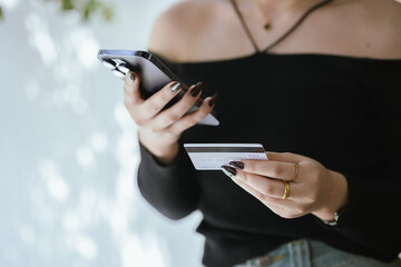 Close-up of young Asian woman using smartphone and credit card for mobile banking or online shopping. She represents modern e-commerce, digital transactions and financial technology.
