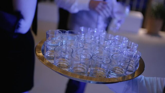 Close up of a tray with filled shot glasses being served at an event under vibrant lighting