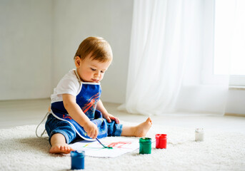 Naklejka premium A toddler draws with colorful paints on a carpet in a sunlit nursery