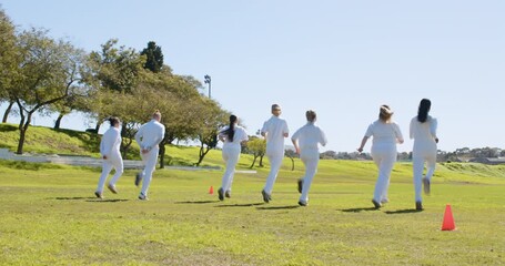 Playing cricket, women in white uniforms practicing on grassy field
