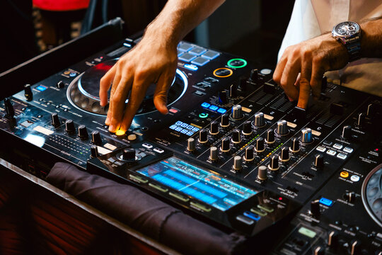 A DJ skillfully manipulates a mixing console, blending tracks to create an electrifying atmosphere at a lively event. DJ mixer controller panel for playing music and partying.