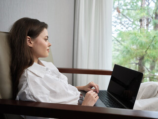 Young woman in casual white shirt working on laptop at home, enjoying a peaceful moment with nature...