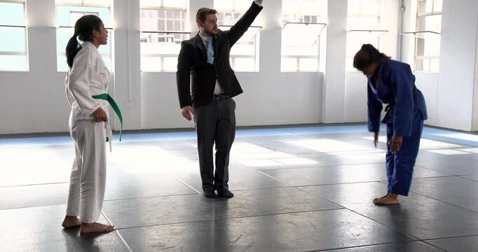 Practicing judo, two women sparring in dojo with instructor observing