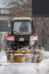 A tractor with a brush cleans the sidewalk from snow on a winter day