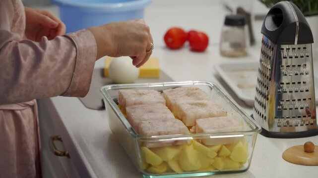 Woman cooking fish cod baked in oven with vegetables at home. Potatoes and cod fish fillet in oven baking dish. Healthy diet healthy food.