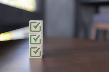 Three wooden blocks with green check marks stacked vertically on a wooden surface, symbolizing...