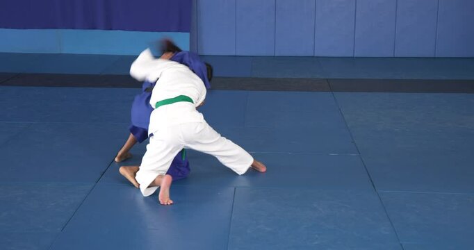 Practicing judo, two athletes in blue uniforms grappling on mat