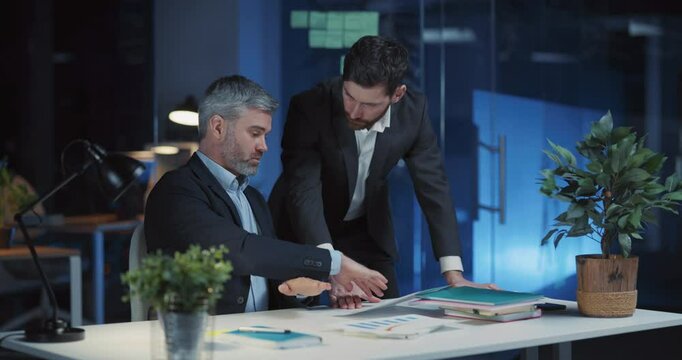 Caucasian team of two businessmen adults overworking in office solving corporate issues brainstorming marketing strategy together. Collaboration. Night time.