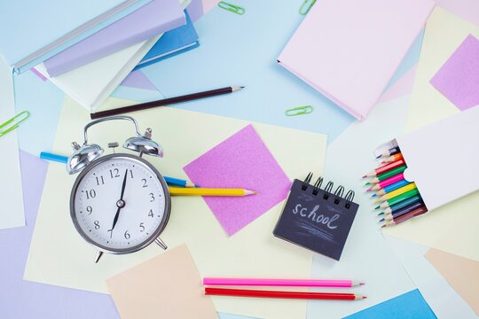 Back to school concept. Alarm clock, notebooks, pencils, paper clips and textbooks on colorful background, pastel colors.