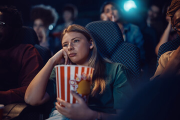 Young woman feeling bored during film screening at movie theatre.