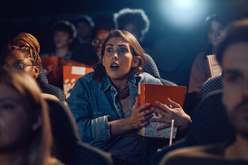 Young shocked woman watching suspenseful movie at cinema.