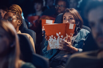 Scared woman watching horror film at movie theatre.