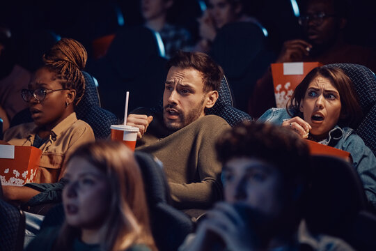 Group of friends watching scary movie at cinema.