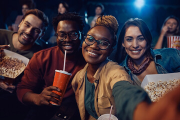 Happy friends taking selfie at cinema and looking at camera.