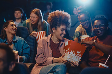Happy woman sharing popcorn with friends while watching movie at cinema.