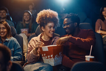 Happy couple sharing large popcorn box at movie theater.
