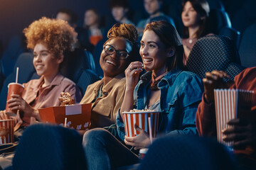Happy female friends enjoying in movie projection at cinema.