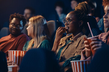 Black woman eating popcorn during movie projection at cinema.