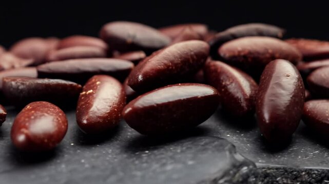 Camera pans right over adzuki beans, rich, dark red, piled high on a dark slate with low key lighting enhancing depth