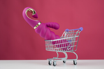 Sex toy in miniature shopping cart on pink background. 