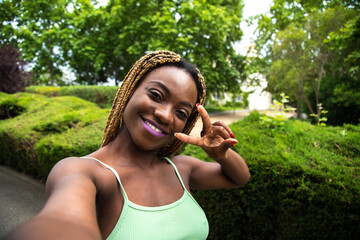 Fototapeta premium Happy Black woman, runner taking selfie while running outdoors in the park looking at camera. Copy space.