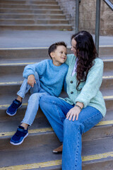 A joyful young boy sits on the stairs, engaging playfully with his mother, who beams with a warm smile, beautifully showcasing the loving bond they share during this special moment together in time