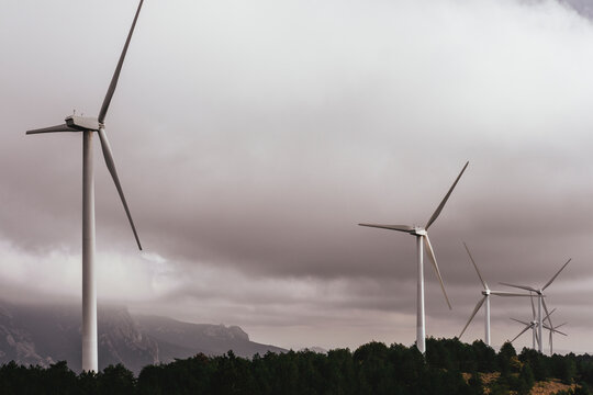 The image features wind turbines standing tall amidst a moody, cloudy sky, representing sustainable energy amidst the challenges posed by nature and climate change in Navarra Spain