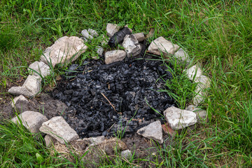 Charred remains of a campfire surrounded by stones in a grassy area after use during a summer evening