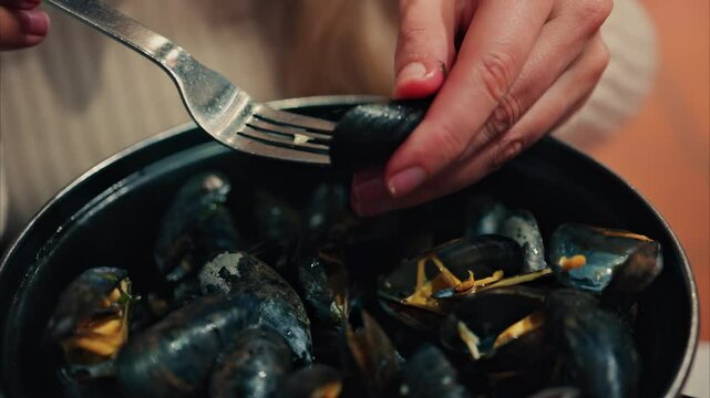 Close up of a woman eating mussels from a pan with a fork
