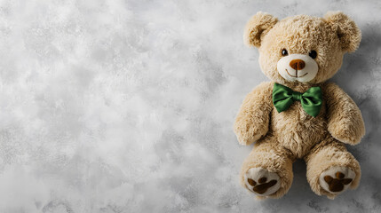 A soft teddy bear wearing a green bow tie stands against a clean, light gray backdrop, offering an adorable focal point perfect for designs with ample copy space.