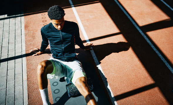 High angle view of a fit young man in sportswear doing a leg workout using a foam roller on the floor of a sunny gym