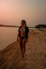 Young Brazilian woman in swimwear walking along a serene beach at sunset