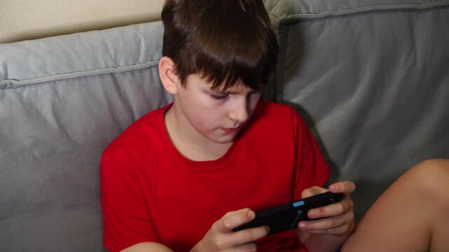 ten year old boy playing smartphone sitting on sofa