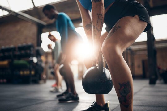 Fit woman swinging a kettlebell during a gym workout class. She stands in a row, next to her friends. A ray of sunlight comes in through the window