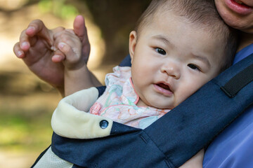 Baby girl is being carried in a baby sling by her mother and holding his finger