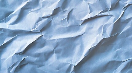 Obraz premium A wrinkled sheet of blue paper lies in soft light, illustrating a blend of shadows and textures that evoke a sense of depth and creativity in its chaotic elegance.