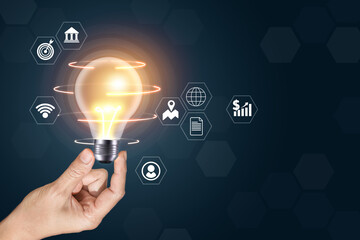 A hand holding a light bulb with a bunch of icons around it. The icons include a bank, a person, a globe, a book, a dollar sign, and a wifi symbol