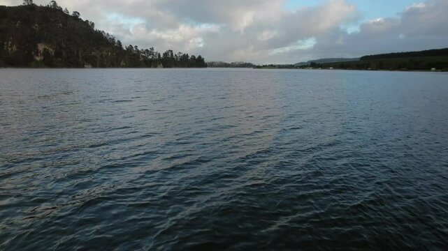 Drone flight skimming over calm reservoir waters near Whakamaru Dam, surrounded by natural landscapes and serene skies. Represents New Zealand's harmony with nature and water conservation efforts.