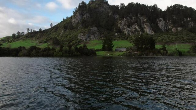 Whakamaru lake with rocky hills, trees, and green fields in Waikato, New Zealand