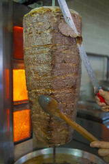 Close-up of a chef cutting meat with a doner knife for the traditional Turkish dish meat doner or...