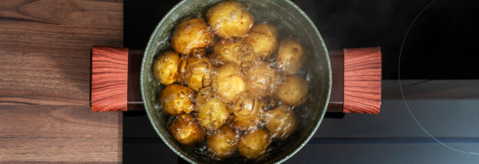 Baby potatoes in green pot boiling and steaming in water on induction hob