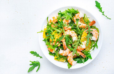 Shrimp salad with orange, arugula and sesame seeds on white background. Top view