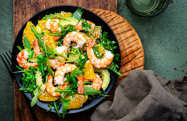 Delicious shrimp salad with avocado, orange, arugula and sesame seeds on green table background. Top view