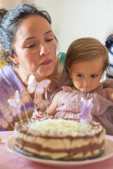 Mother and her one-year-old baby girl are celebrating a birthday with a chocolate and white chocolate layered cake decorated with butterfly candles