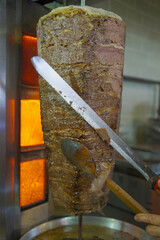 Close-up of a chef cutting meat with a doner knife for the traditional Turkish dish meat doner or...