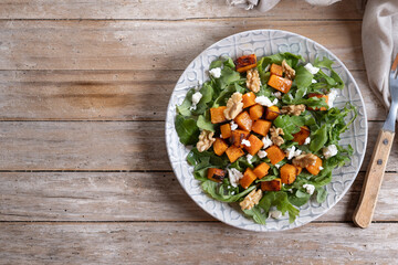 Pumpkin salad with arugula, walnuts and feta cheese on wooden. Top view. Copy space