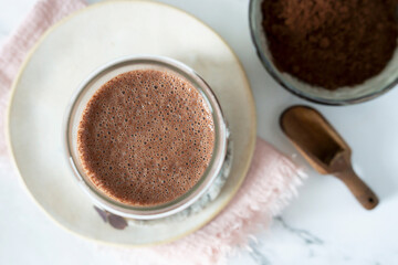 A chocolate protein shake served in a glass, beside it, a small bowl filled with cocoa powder.