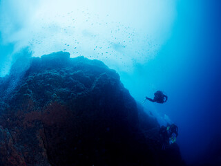group of unrecognizable scuba divers in wetsuit diving near of a rough rocky formation in deep blue sea with clear water, concept of active leisure in ocean and underwater adventure